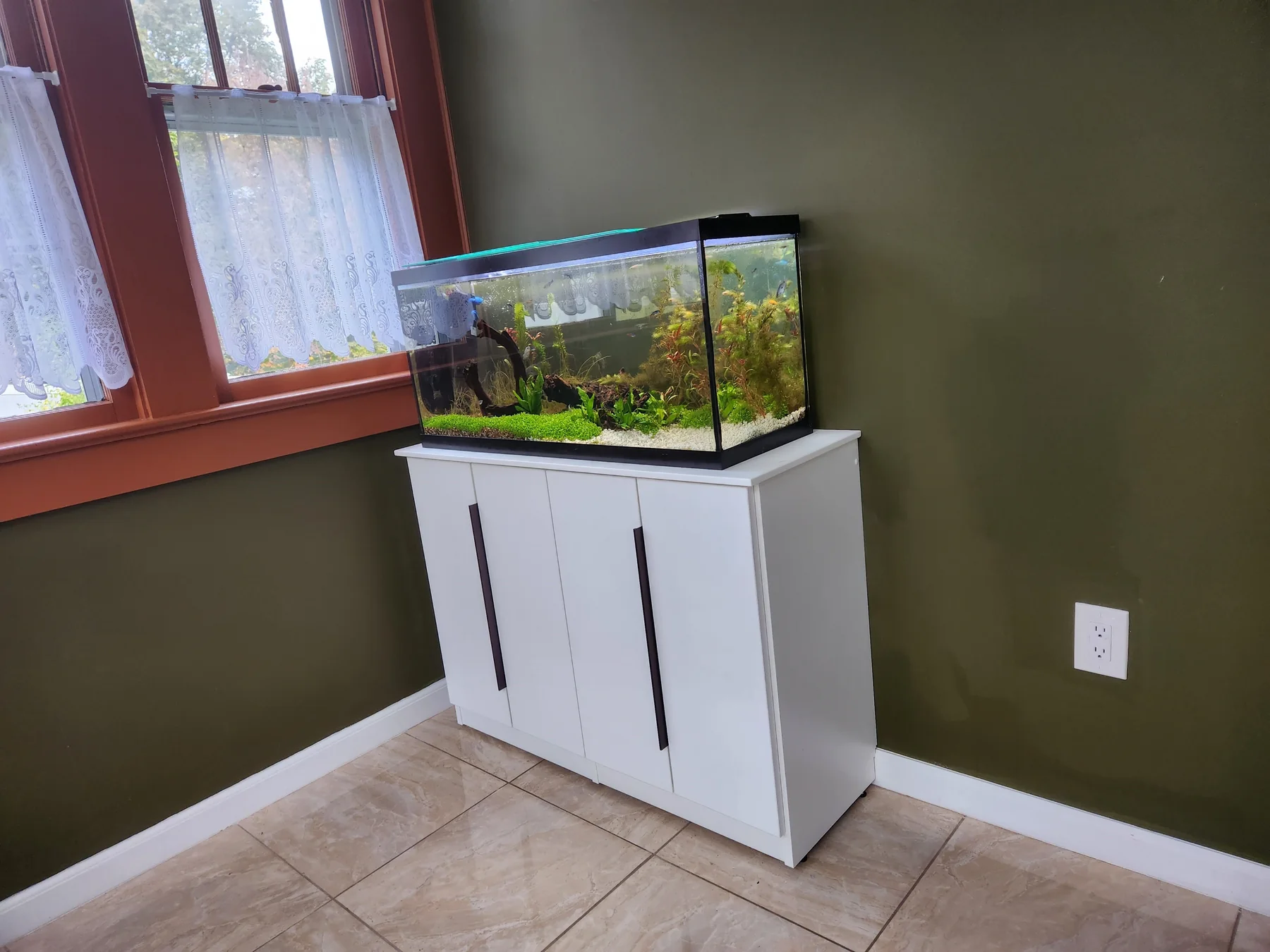 White storage cabinet with slim dark handles supporting a planted aquarium