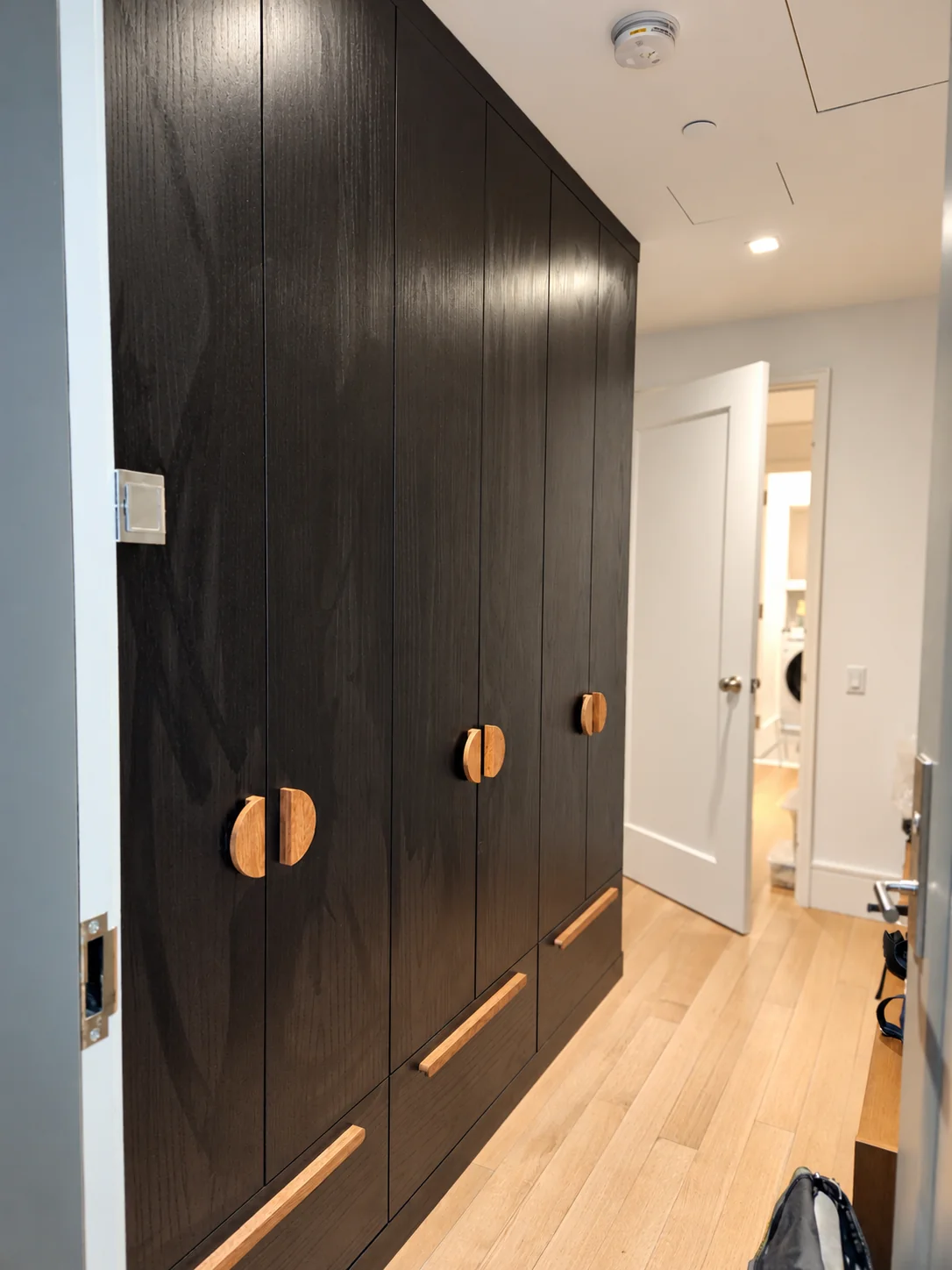 Black wood-grain wardrobe with semicircular wooden door pulls and long wooden drawer handles