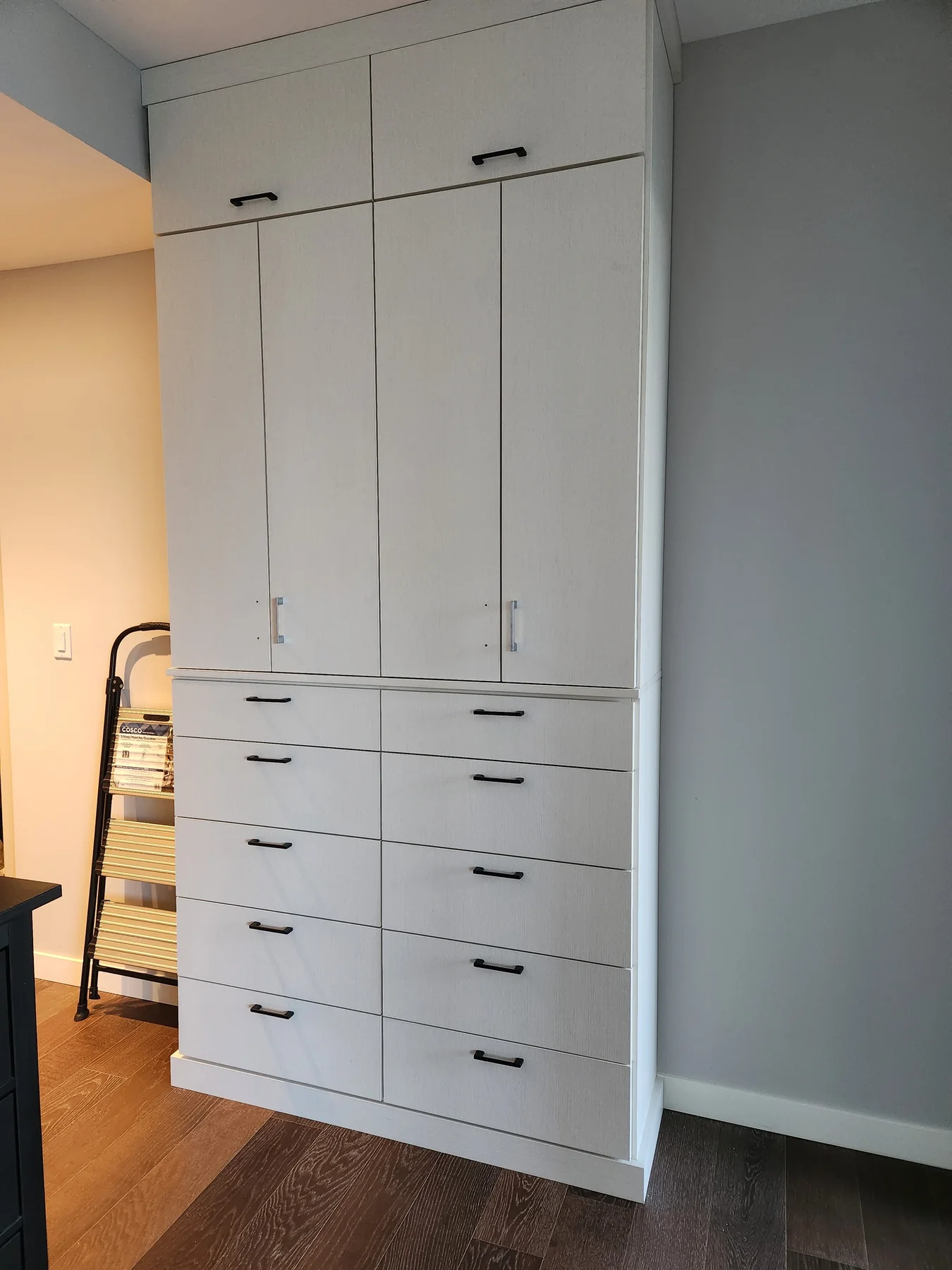 White built-in cabinet with paneled doors, lower drawers and dark handles