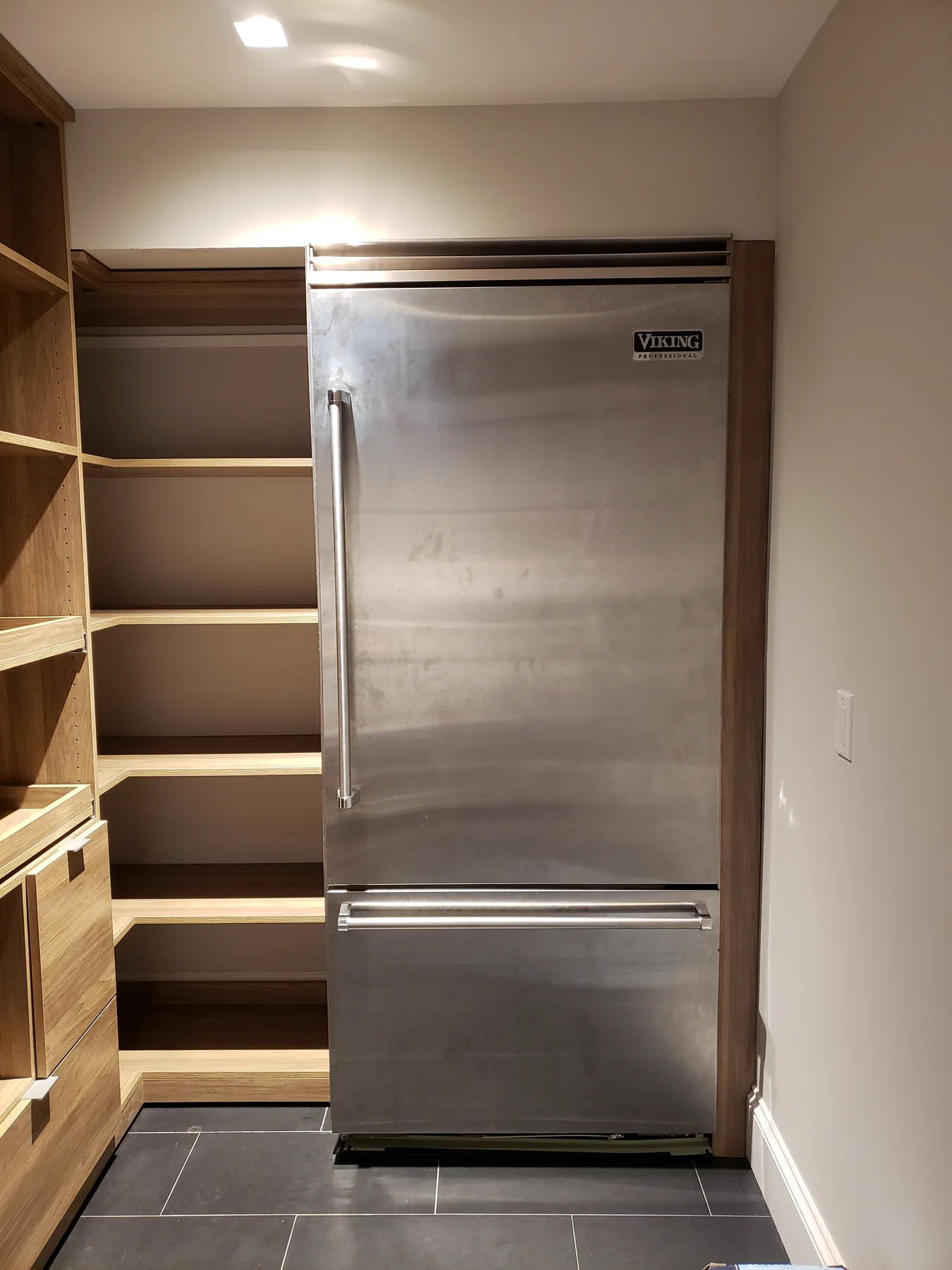Pantry shelving fitted around a tall stainless-steel refrigerator