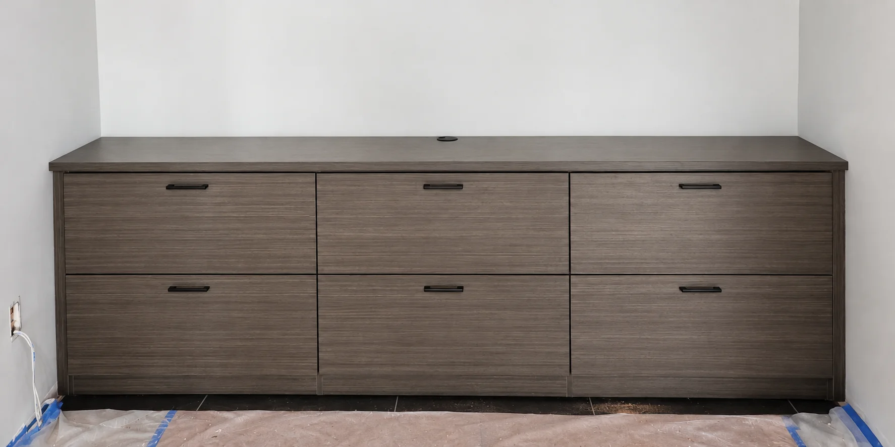 Low wood-grain cabinet with six drawers, dark handles and a cable opening in the top