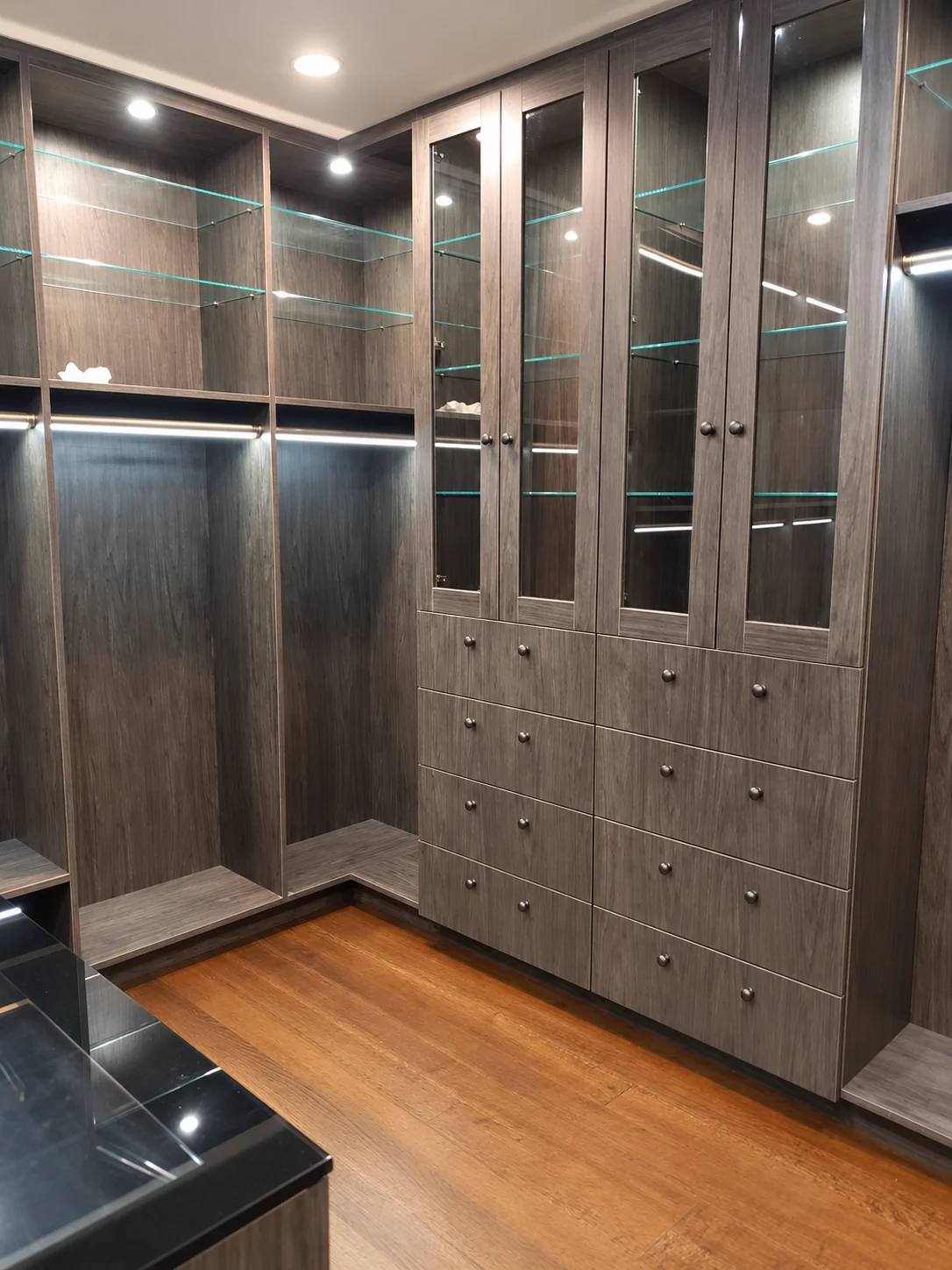 Glass-front wardrobe doors and drawer storage with round knobs beside illuminated hanging sections