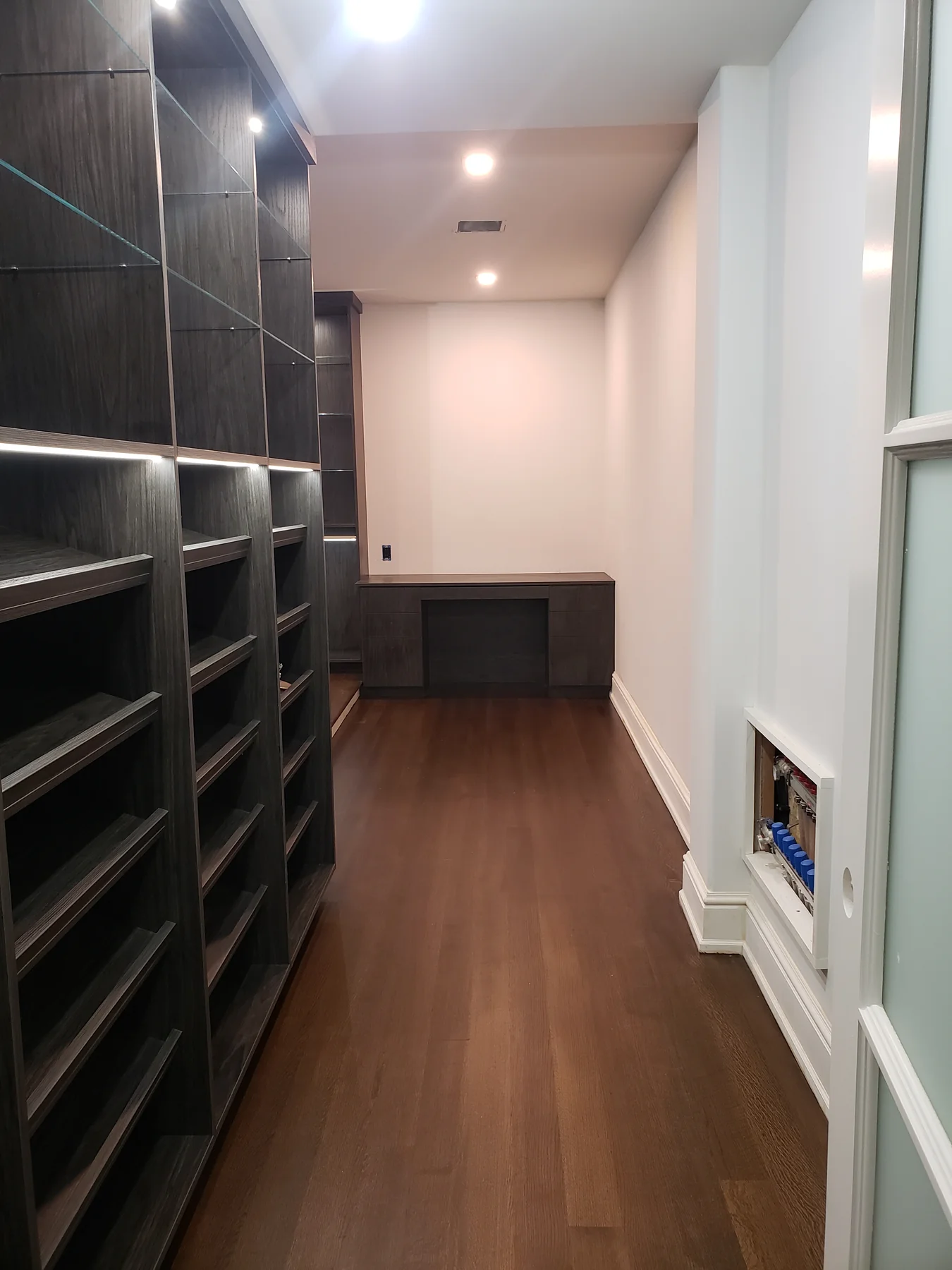 Long closet aisle with glass shelves, shoe shelving and dark wood-grain cabinetry