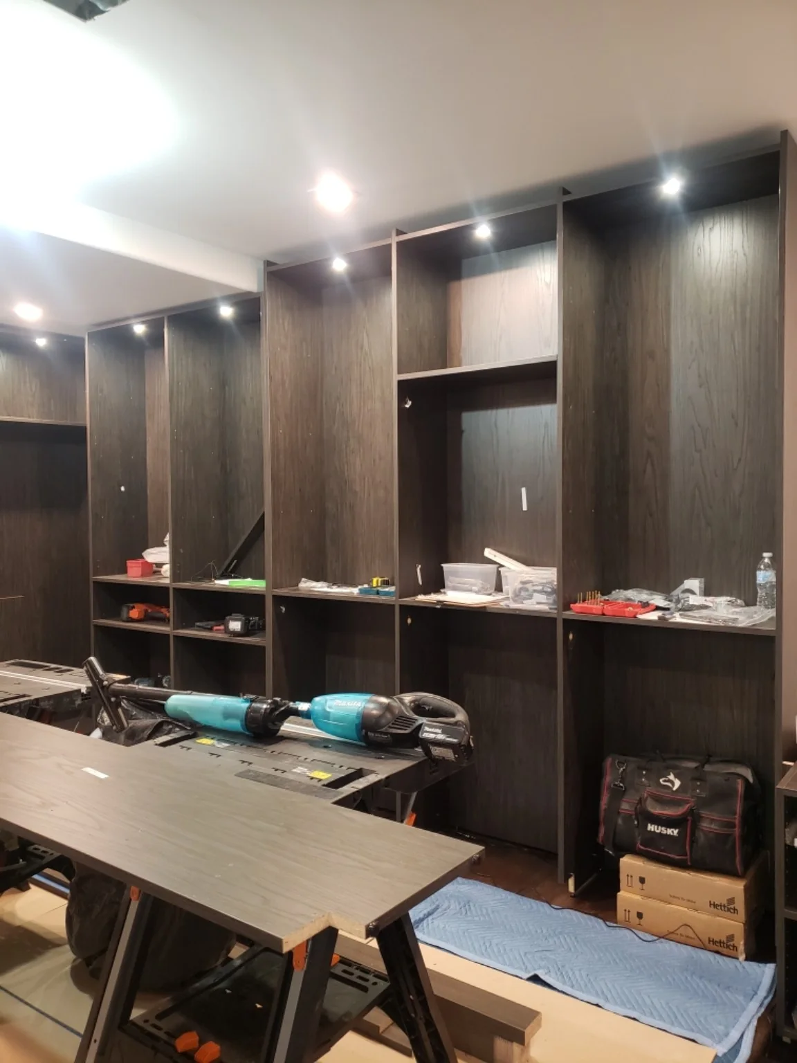 During installation: fitting the dark wood-grain wardrobe cabinets with lighting, before shelves, drawers and glass doors are installed
