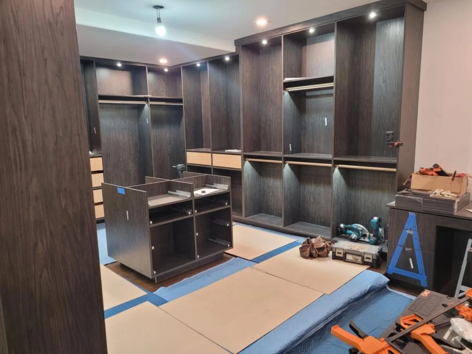 During installation: wide view of the dressing room with the island, hanging rails and wall drawer boxes being fitted