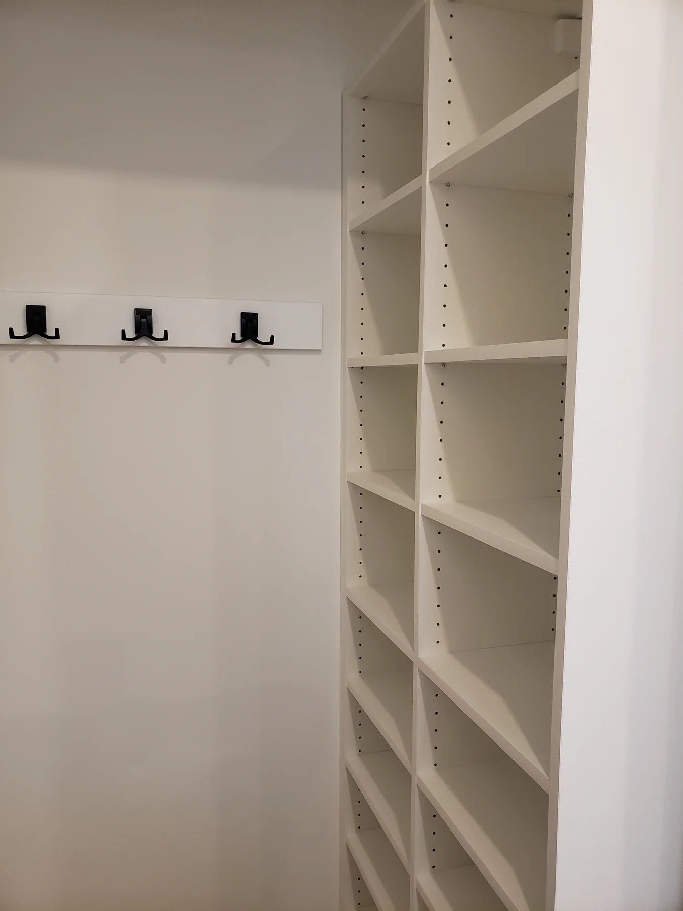 White entry closet with black coat hooks and adjustable side shelving