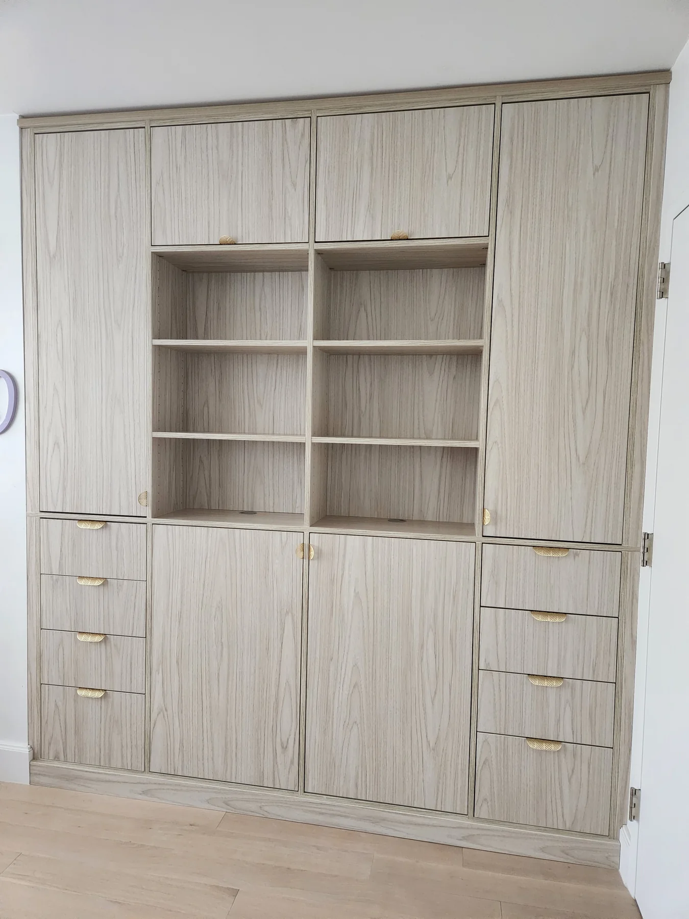 Light wood-finish built-in storage with upper cabinets, open shelves, lower cupboards and drawers