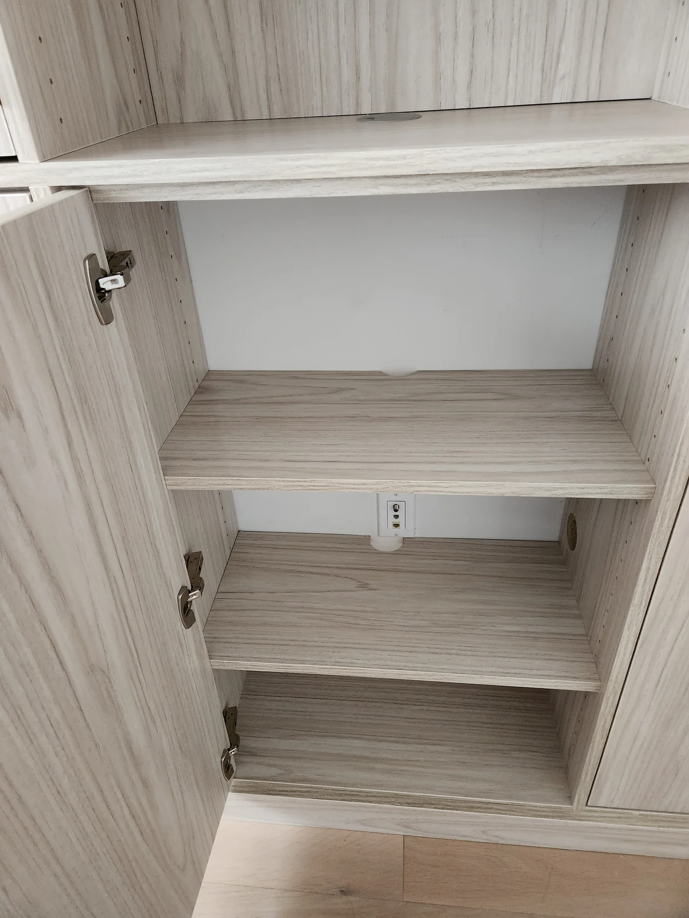 Interior of a wood-finish storage cabinet with shelves and a wall outlet