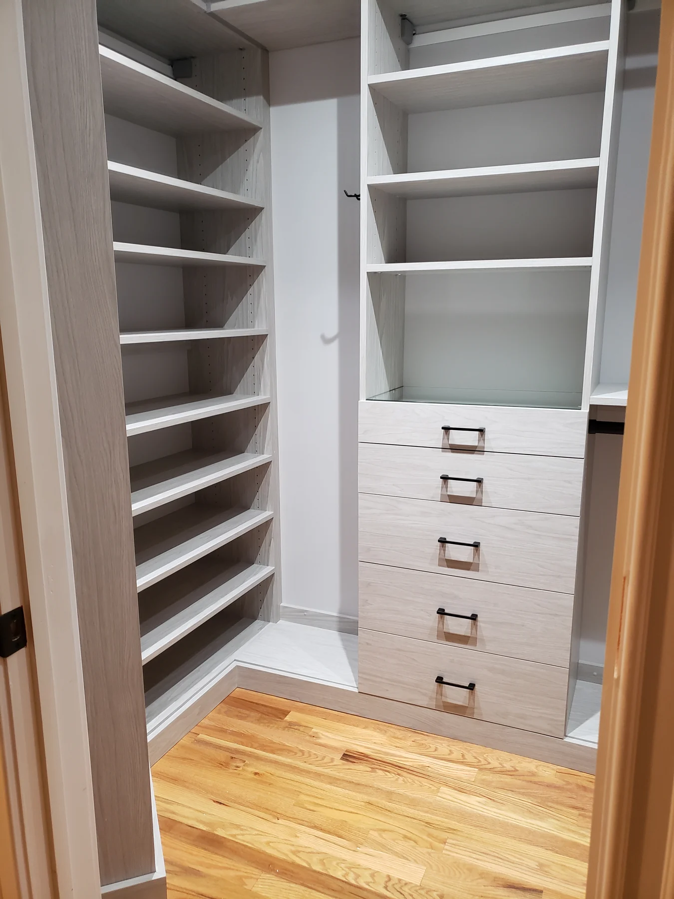 Light wood-grain walk-in closet with a drawer tower, adjustable shoe shelves and hanging space