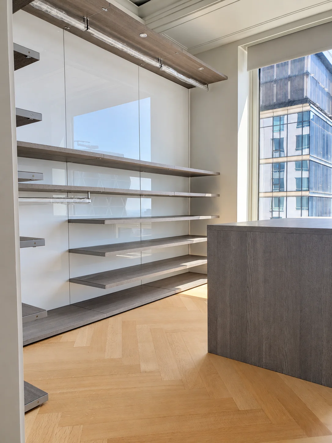 Modern closet with suspended wood-finish shelves, glossy white back panels and an island by a large window