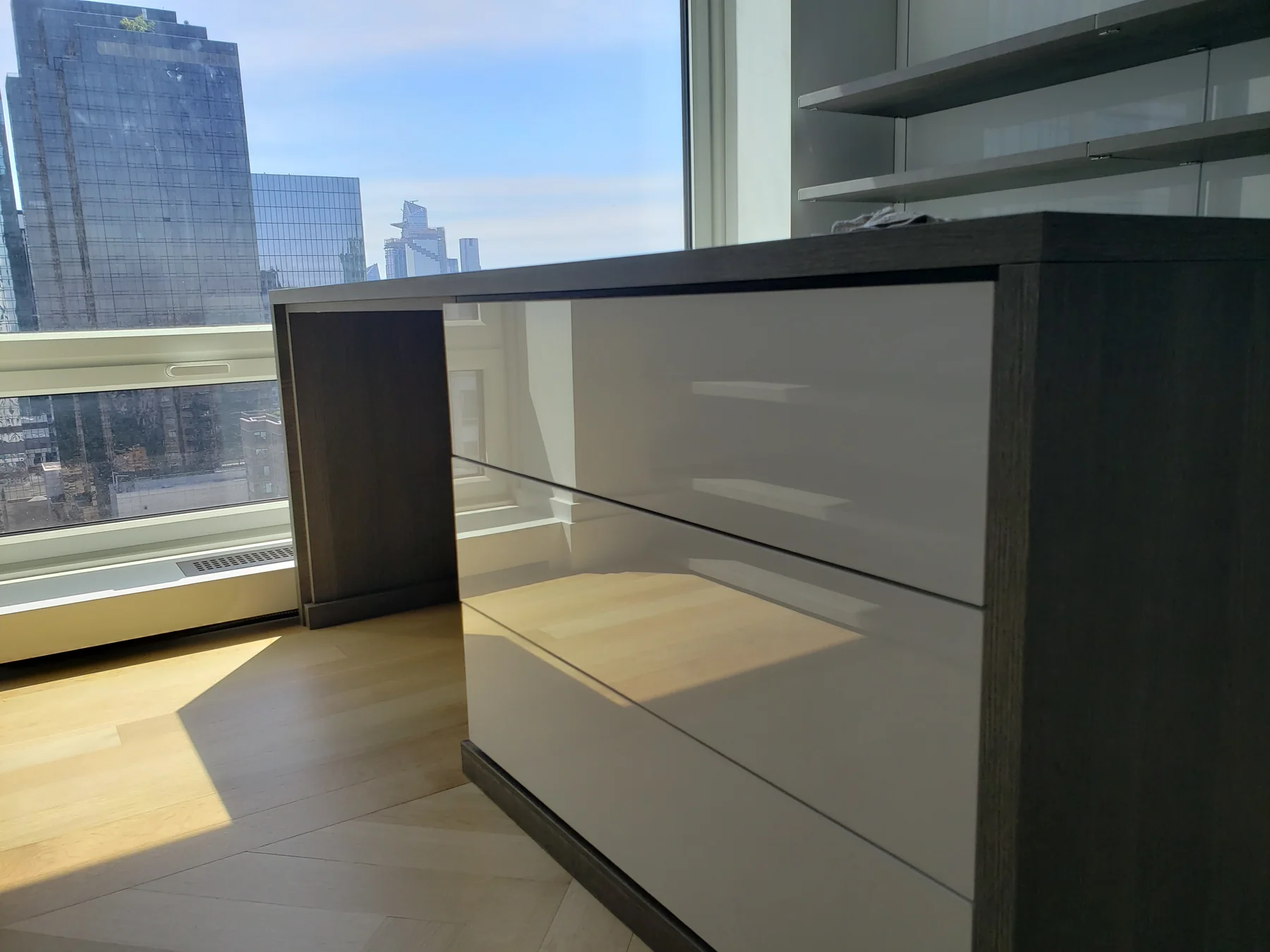 Closet island with glossy white drawer fronts and a dark wood-grain frame beside a window
