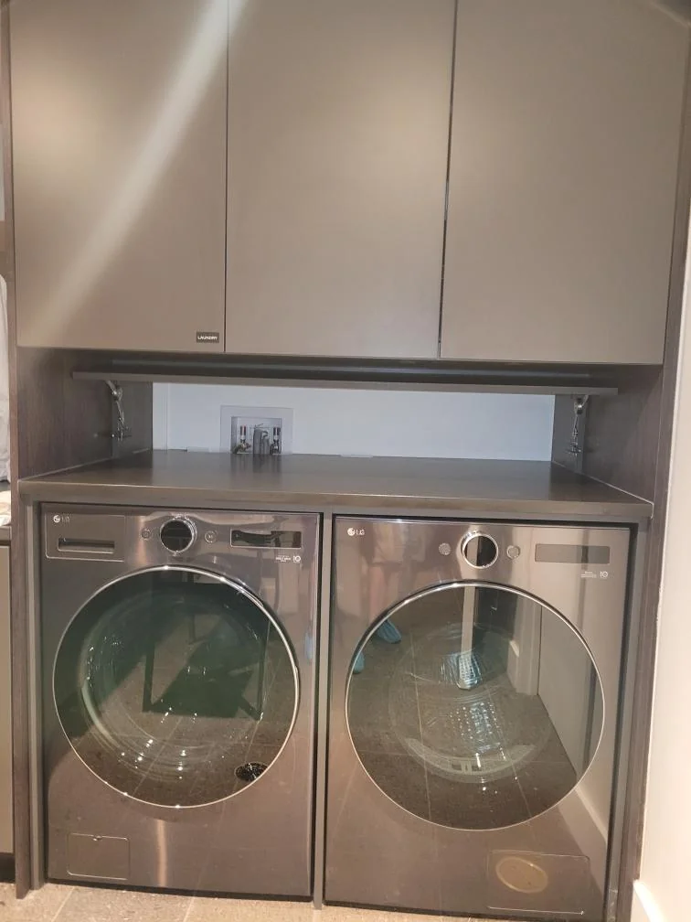 Taupe laundry cabinetry with three upper doors, an open recess and a countertop above a washer and dryer