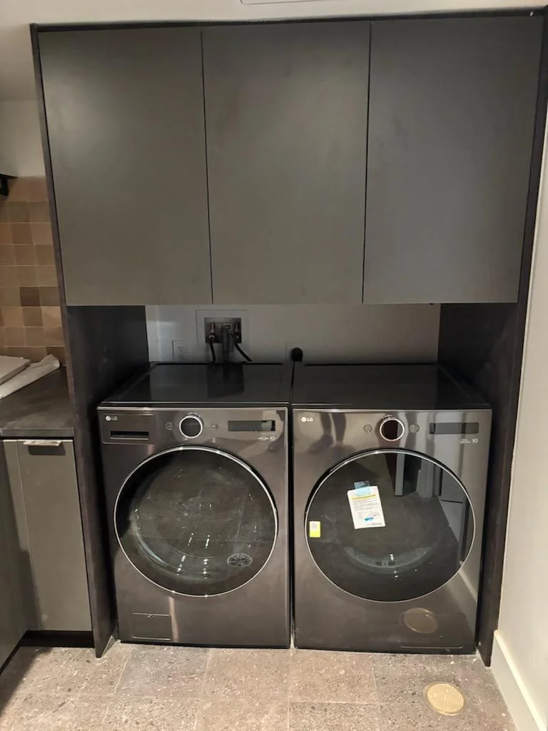 Front view of fitted laundry cabinetry around two stainless-steel appliances beside matching kitchen cabinets