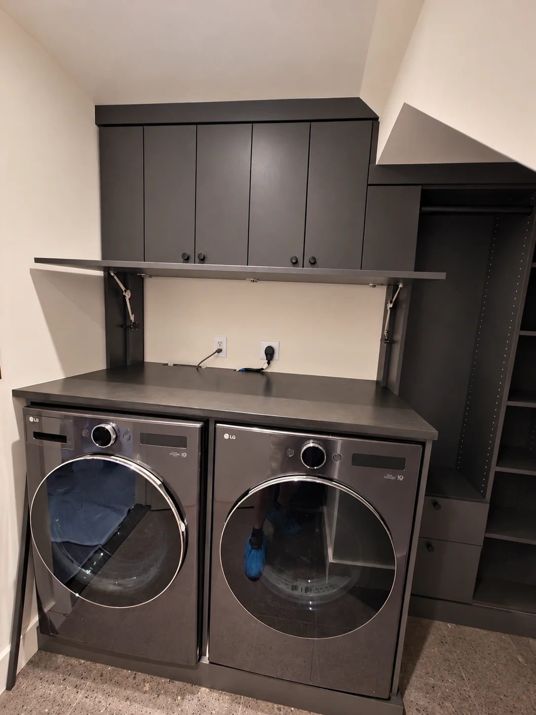 Dark laundry cabinetry with four upper doors, a countertop, a raised hinged panel and tall open storage beside the washer and dryer