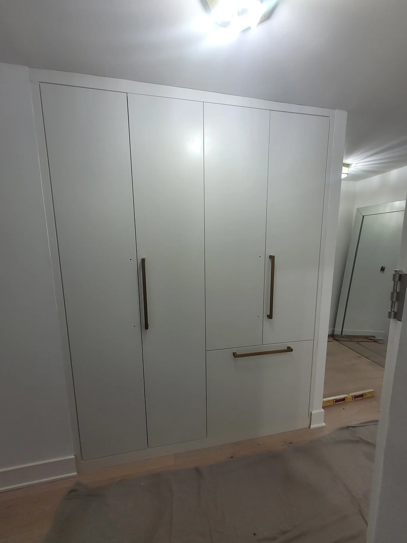 Pale fitted wardrobe with tall paneled doors, long dark handles and a lower storage front