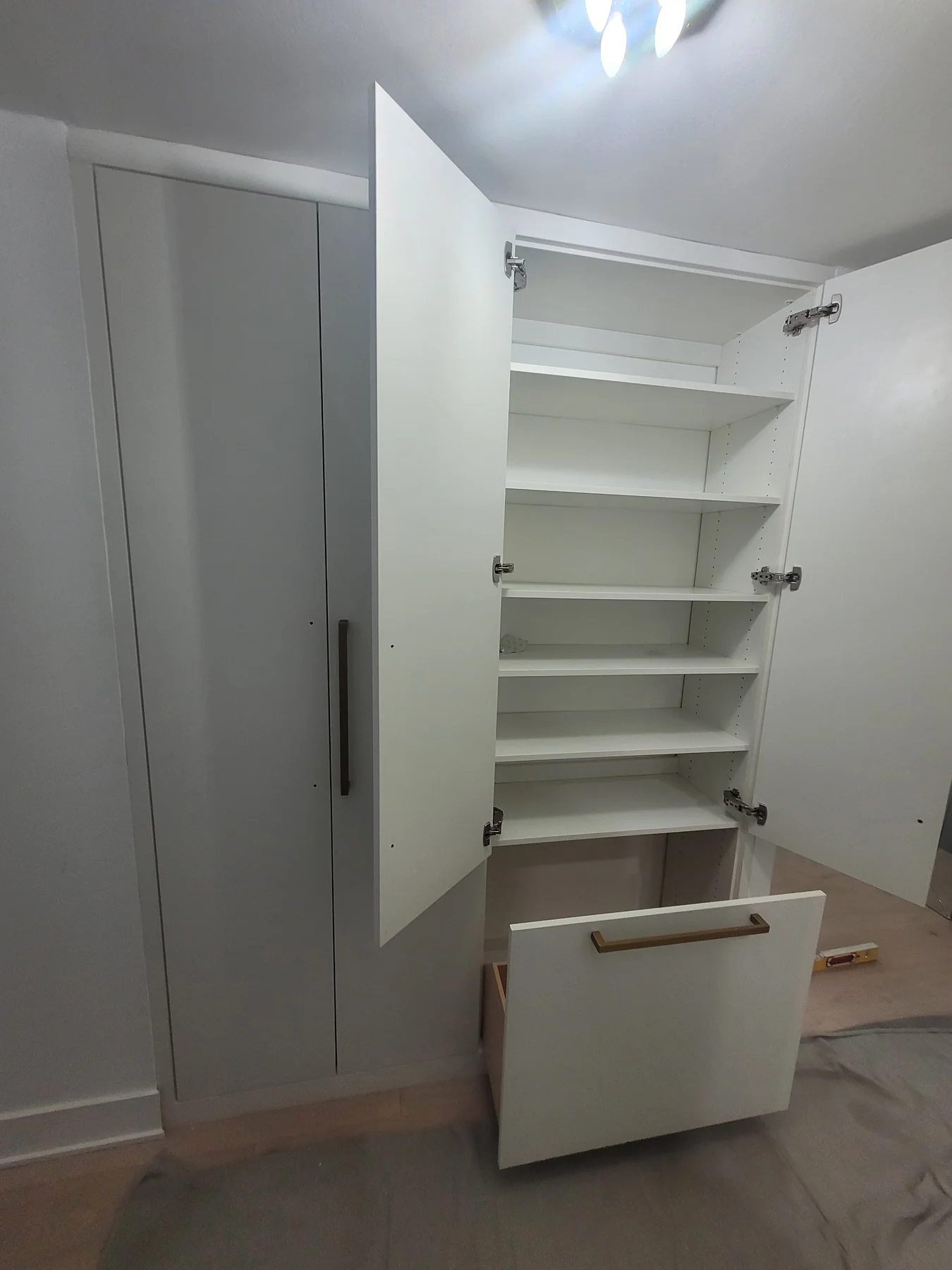 Open fitted wardrobe showing adjustable shelves and an extended lower pull-out shoe-storage unit