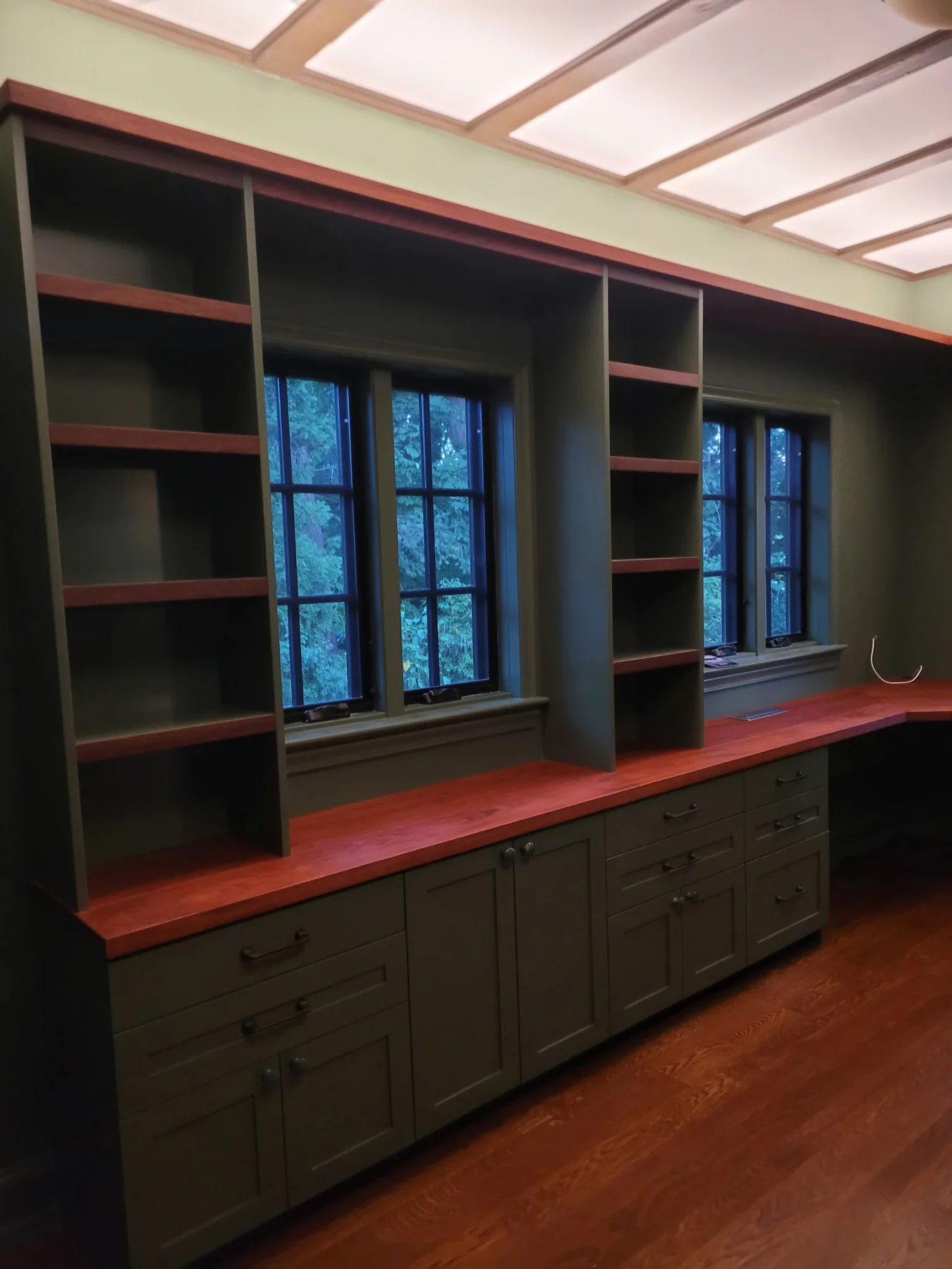 Long wood worktop and olive green storage cabinets beneath two windows