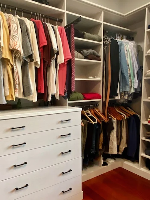 Pale wood-grain closet drawers beneath hanging clothes with corner shelves beside the window