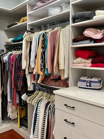 Closet storage with folded clothing, hanging rails, pale wood-grain drawers and dark handles