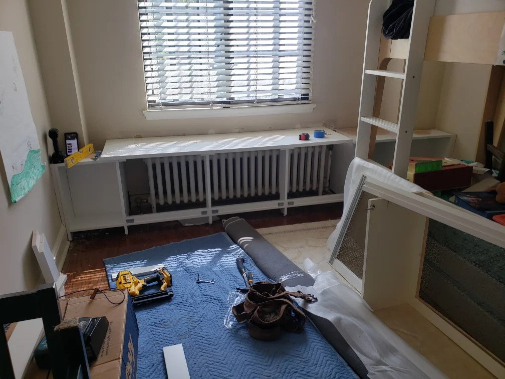 During installation: fitting the long radiator enclosure beneath a window before the decorative front panels are installed
