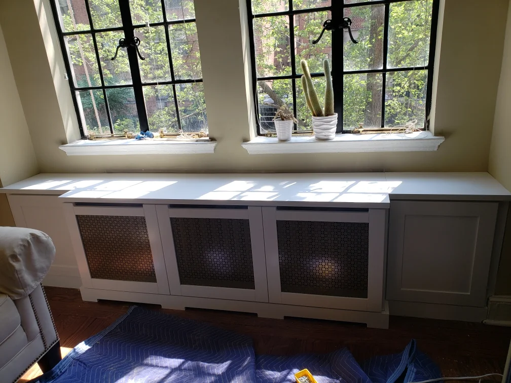 During installation: decorative radiator panels being fitted beneath two windows while the floor remains protected