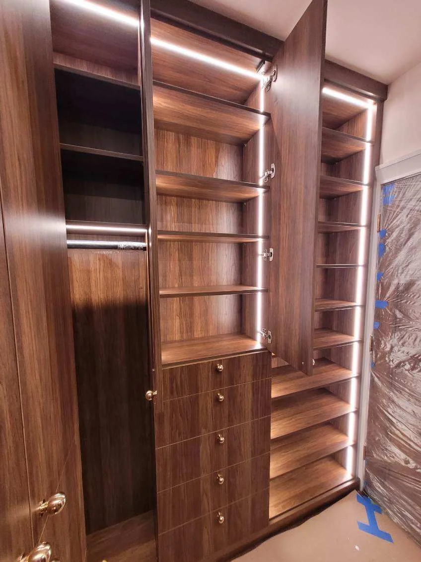 Wood-grain closet drawer stack with round knobs beside a tall shoe-shelving tower and illuminated hanging section