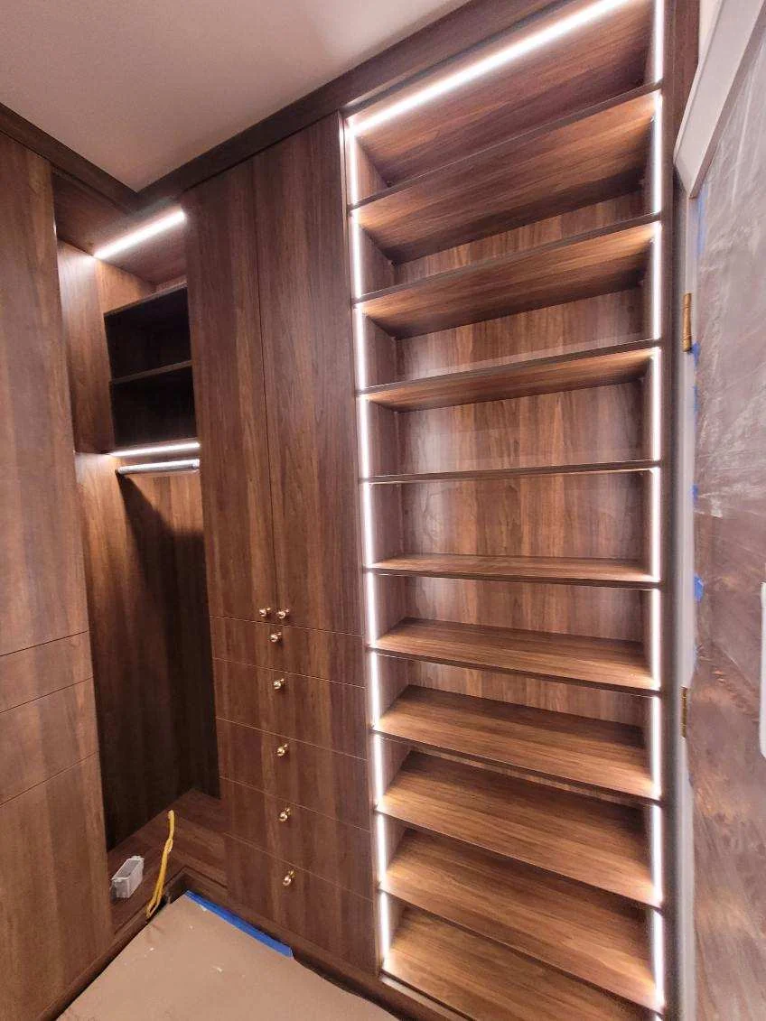 Tall shoe shelves and hanging storage with integrated lighting in a wood-grain walk-in closet