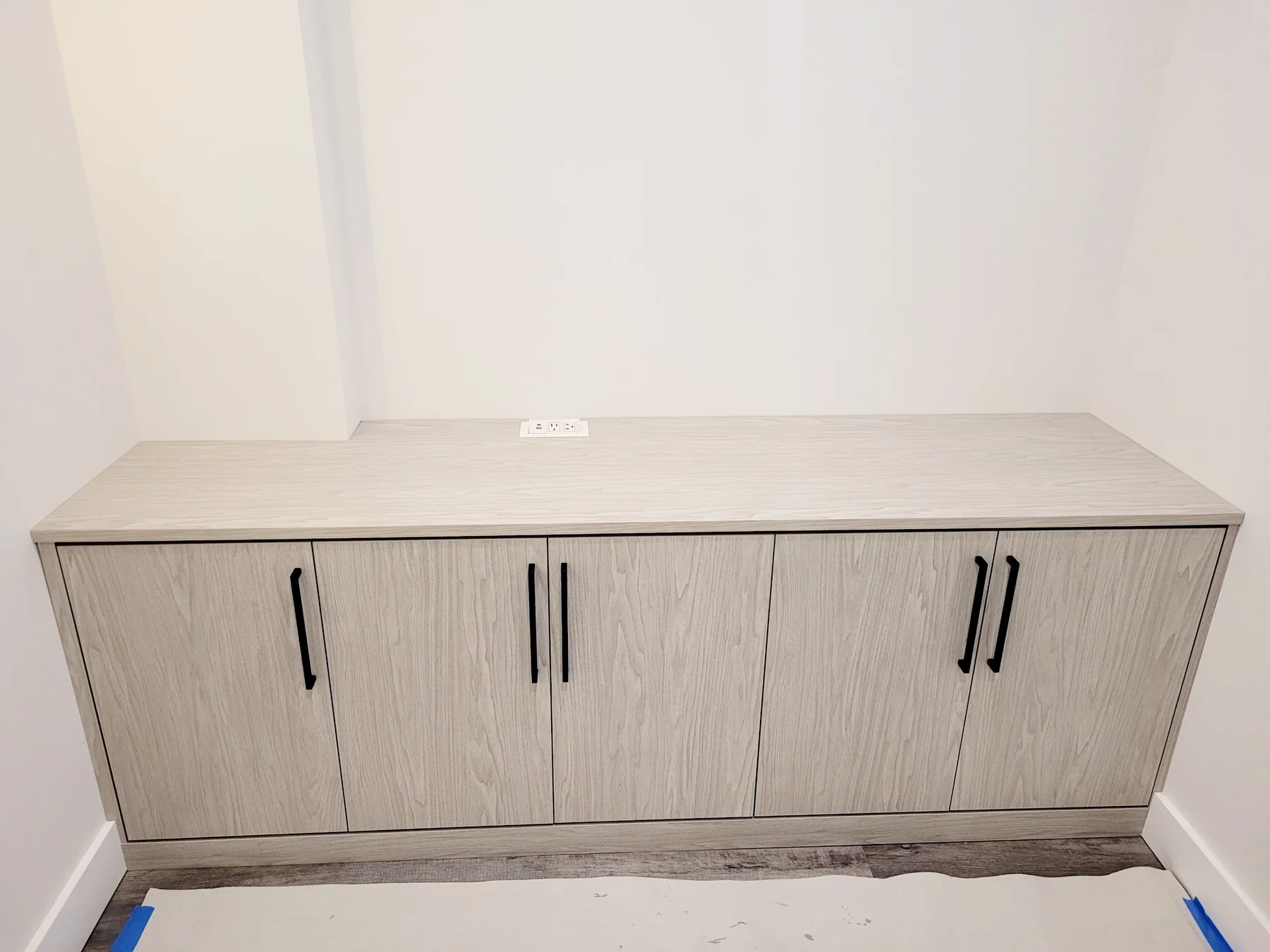 Low light wood-grain sideboard with four doors, slim dark handles and a concealed power module in the countertop