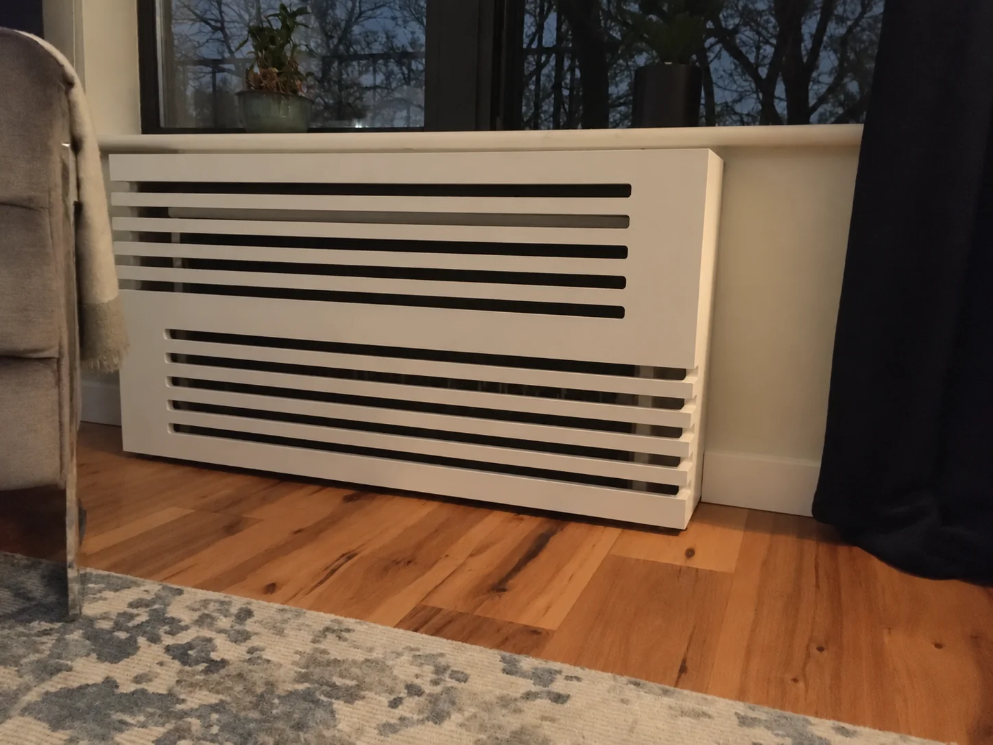 White radiator cover with horizontal ventilation slats beneath a window
