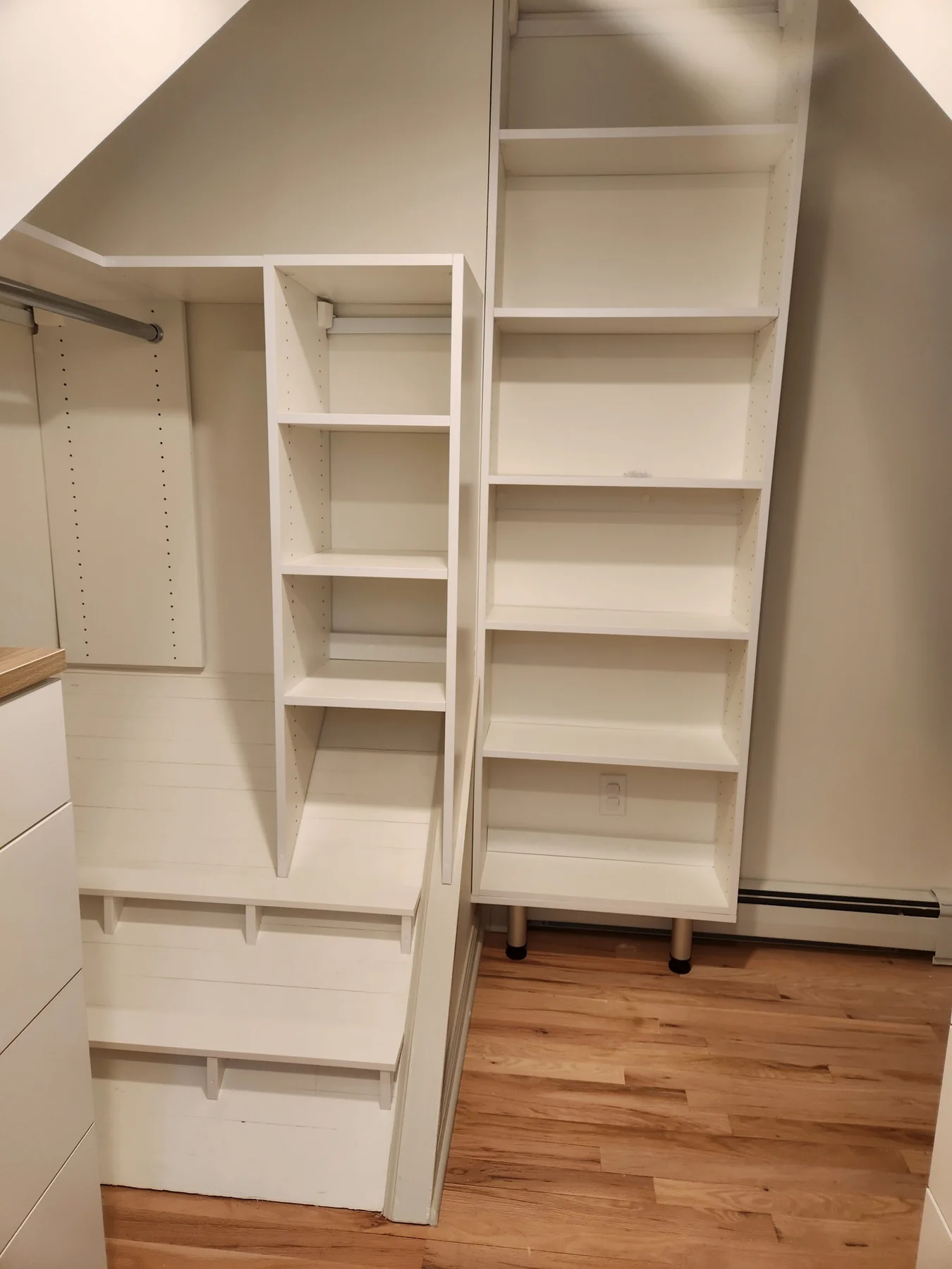 White shelving and hanging rails arranged around an angled ceiling
