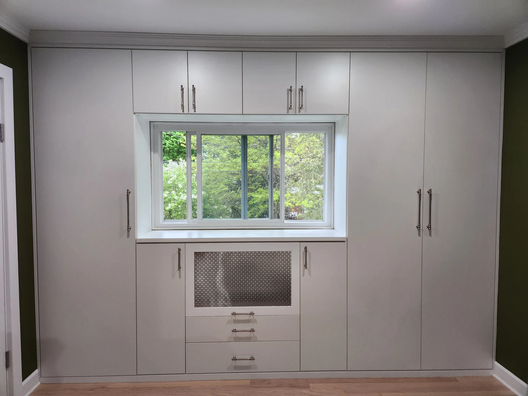 White built-in wardrobe surrounding a window with doors, drawers and a central display compartment