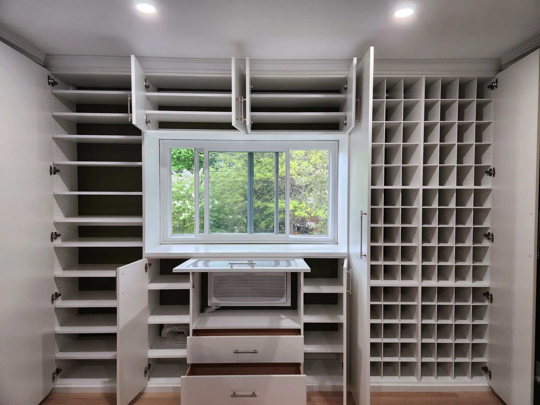 Open wardrobe doors reveal adjustable shelves, hanging storage and shoe cubbies around the window