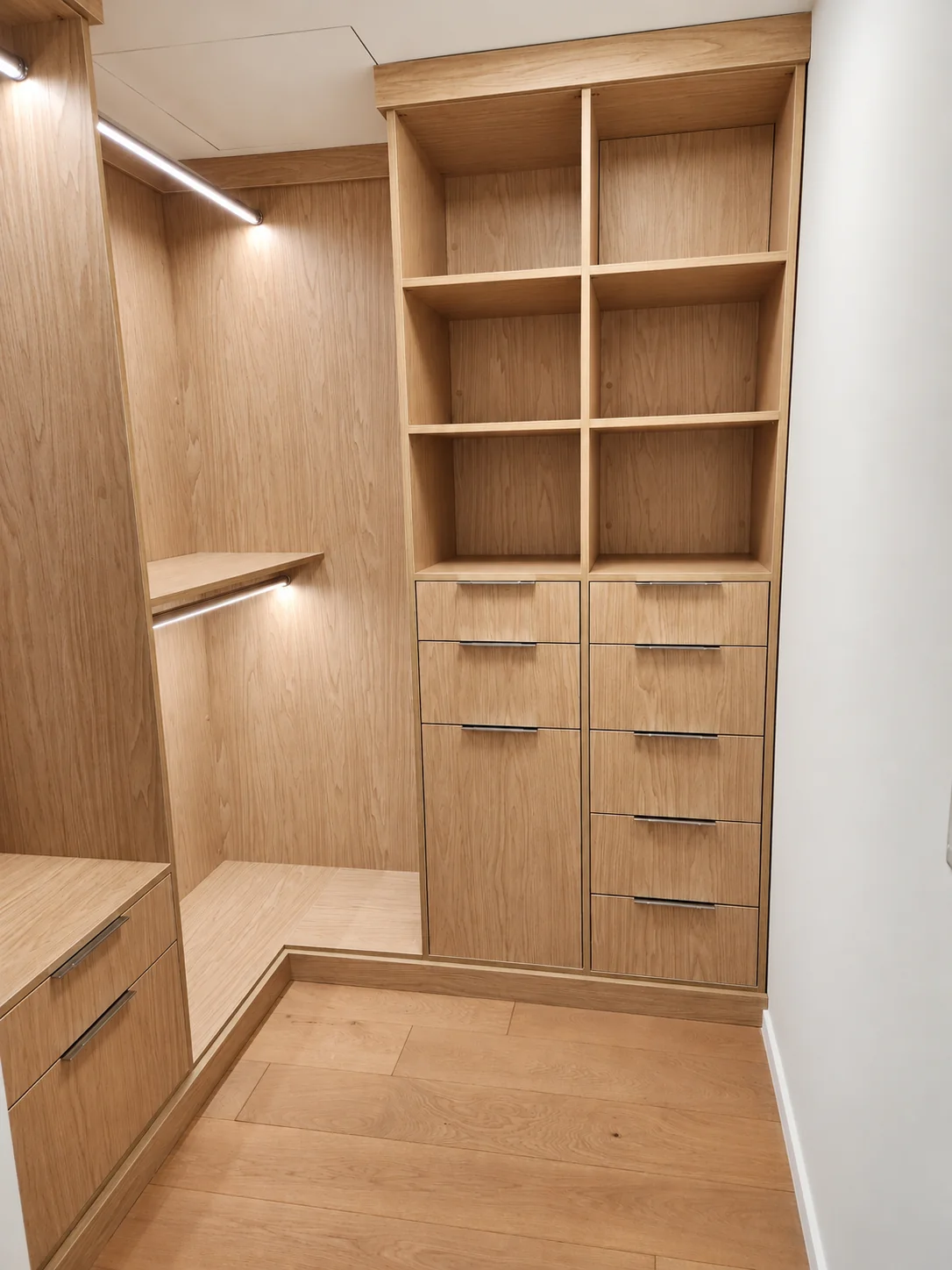 Warm wood-finish walk-in closet with six open cubbies, drawers and illuminated hanging sections