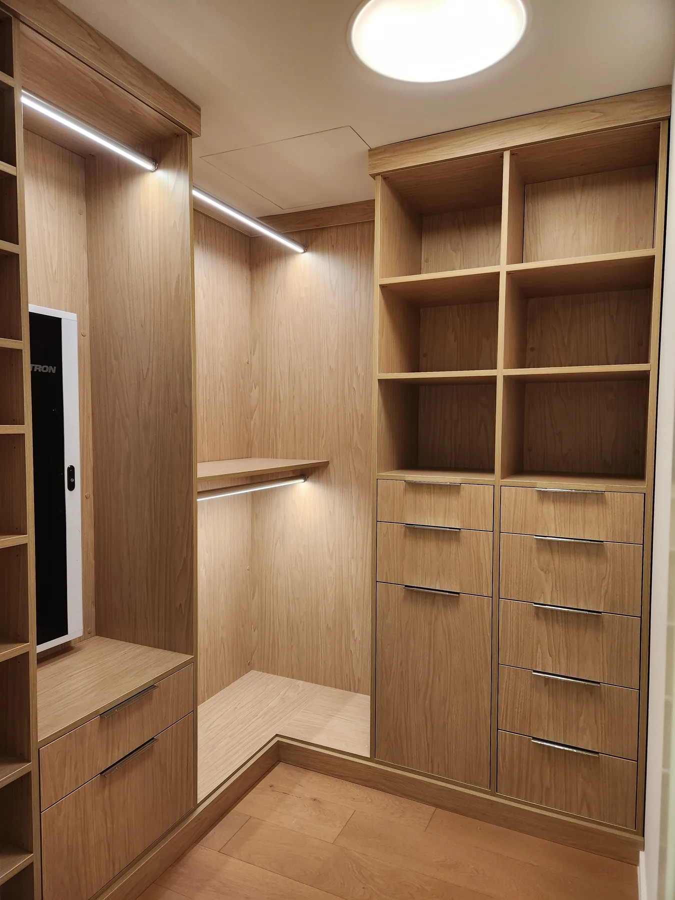 Walk-in closet overview with drawers, open shelves and illuminated hanging rails