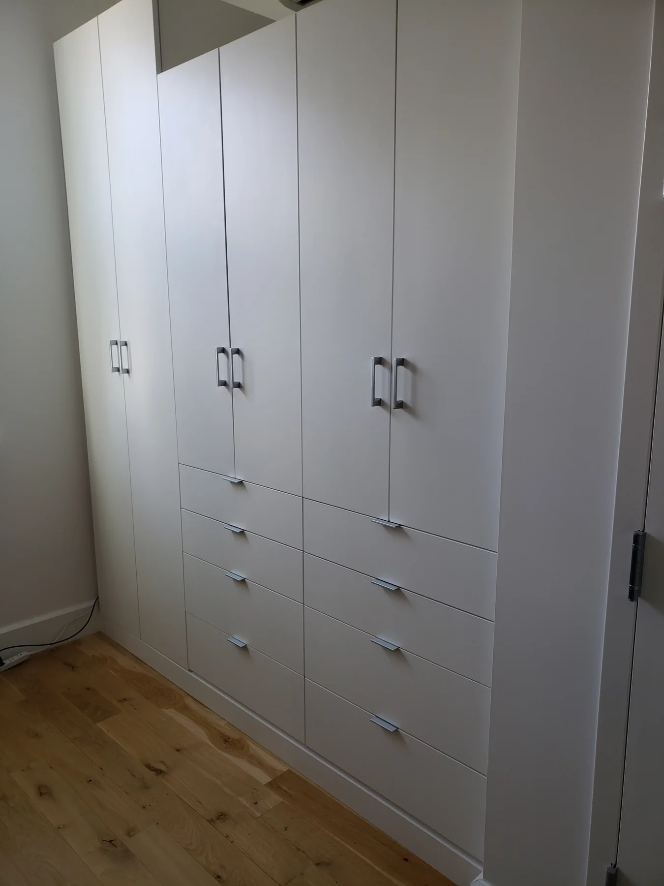 Full-height white fitted wardrobe with paneled doors, lower drawers and metal pulls