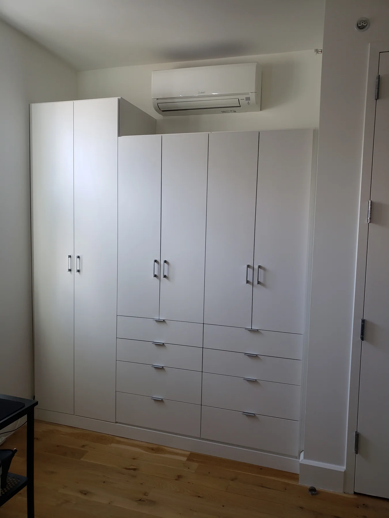 White wardrobe fitted beneath a wall-mounted air-conditioning unit