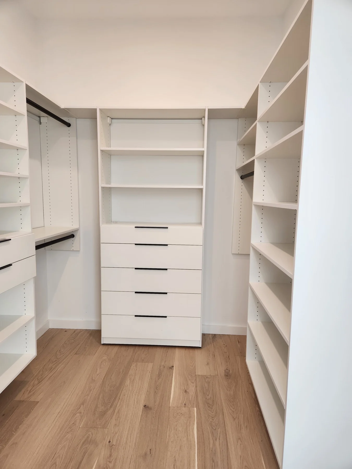 White drawer tower and shelves at the end of a compact walk-in closet