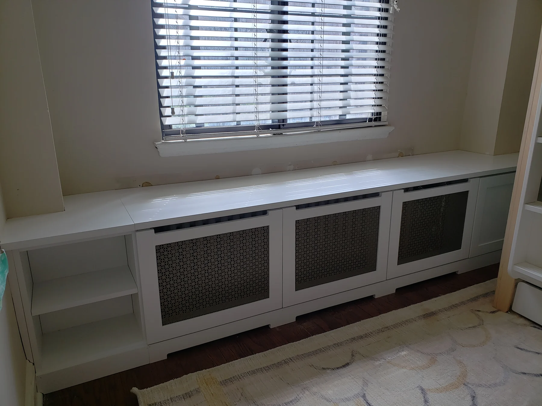 White window-side radiator enclosure with decorative ventilation panels and open side storage