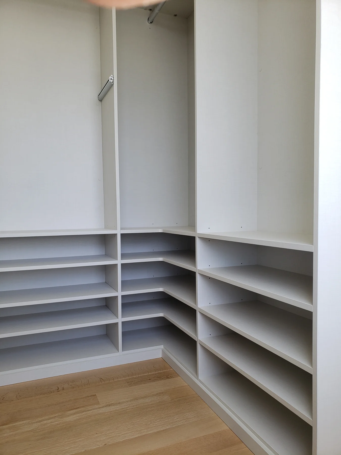 Pale gray closet with hanging rails and low shoe shelves arranged around a corner
