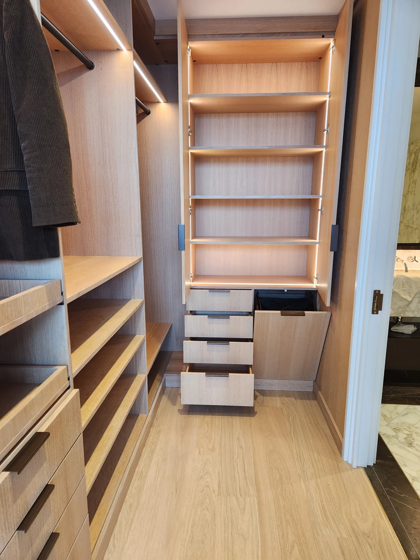 Open closet drawers and shelving in a narrow wood-finish walk-in closet